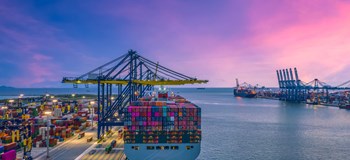 Container ship being unloaded by a crane in port, with a deep purple sky