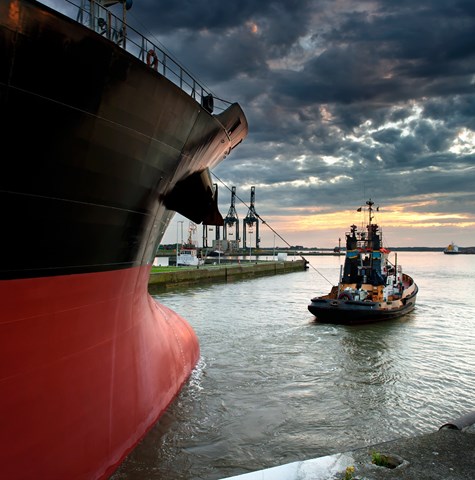 A tug boat guiding a large container ship out of a port